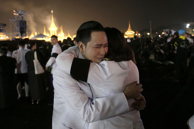 Thailändische Beamte umarmen sich in Trauer als der Rauch aus dem crematorium hochsteigt. (AP Photo/Wason Wanichakorn)