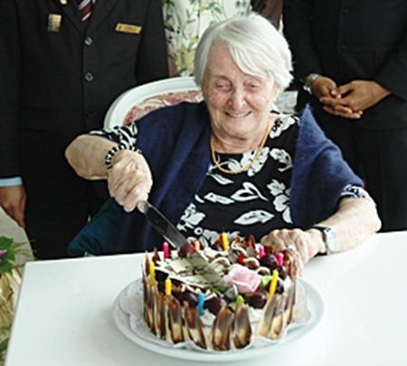 Herta schneidet fröhlich die Geburtstagstorte zu ihrem 99. Geburtstag an.